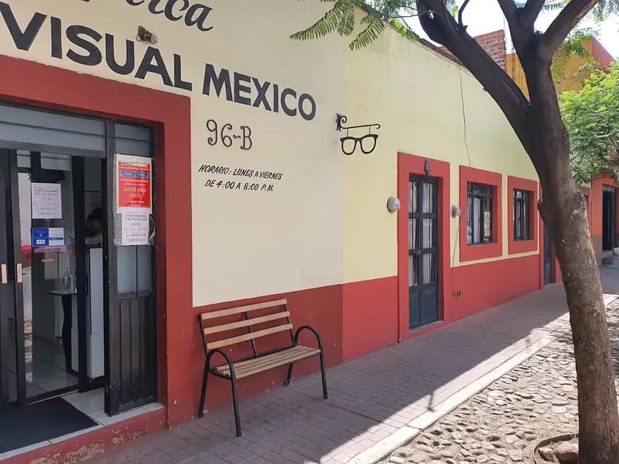 Costado del local de Alianza Visual México con banca de madera y calle empedrada del Centro de Guadalupe