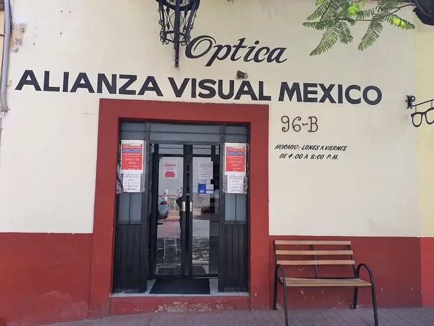 Fachada de Alianza Visual México: muro crema con letras pintadas a mano, marco terracota y letrero de lentes en herrería